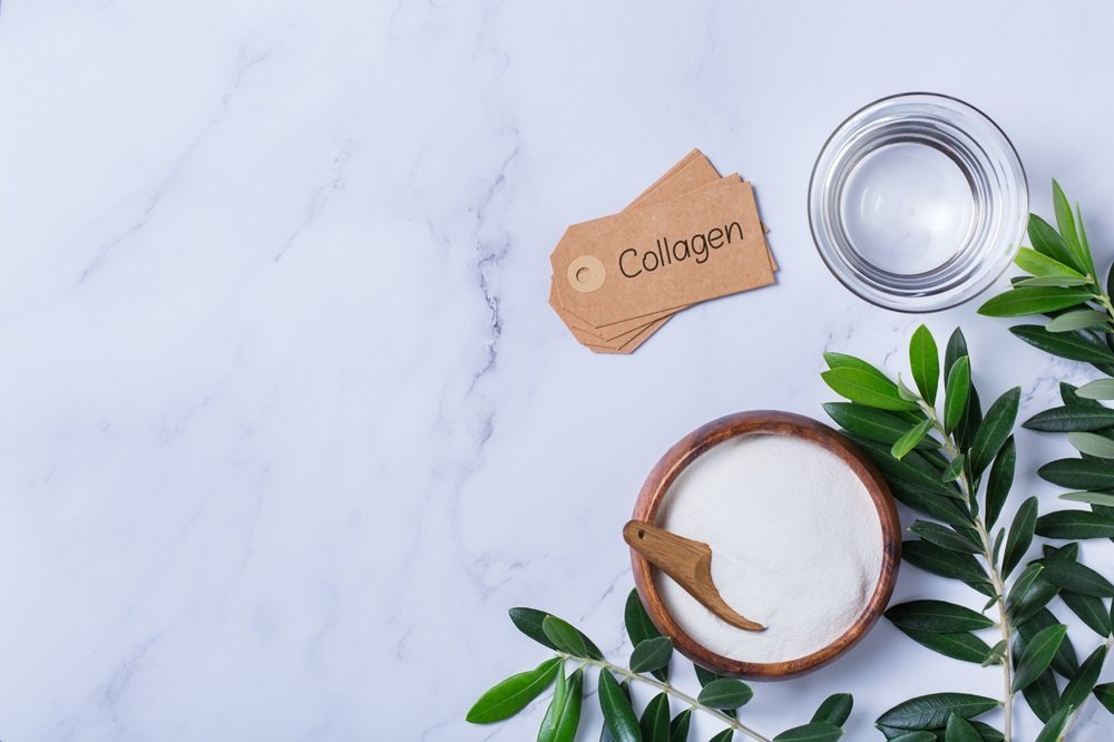Collagen powder on a trendy marble background with green olive tree leaves. Natural beauty and health supplement, wellness skincare anti-aging concept. Top view, flat lay, copy space